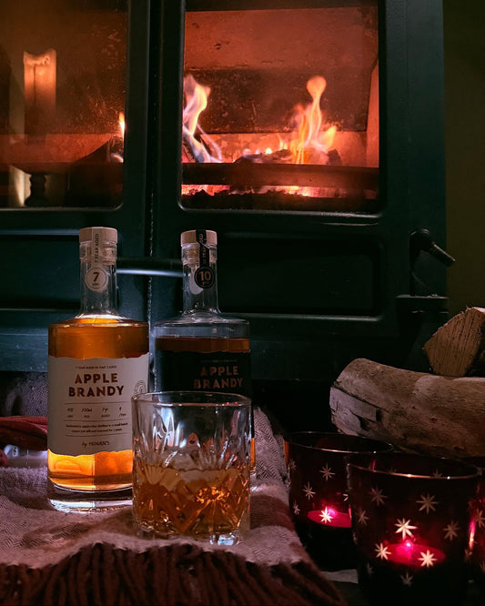 Two bottles of apple brandy with a glass filled with brandy in front of a fireplace.