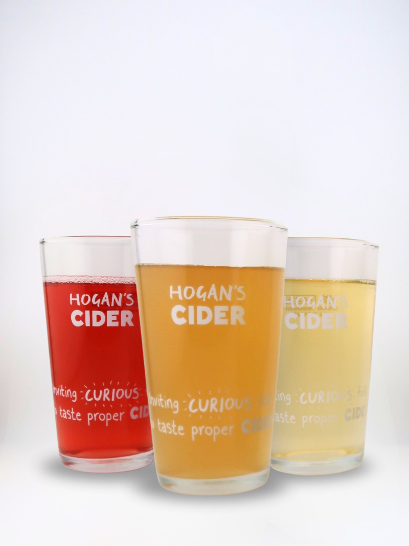 Three Hogan’s Cider half-pint glasses filled with golden and rosy craft ciders, showing our ‘Inviting Curious Folk’ design.