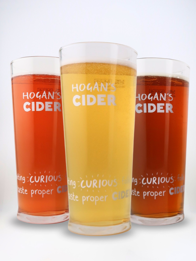 Three Hogan’s Cider pint glasses filled with golden and amber craft ciders, showing our ‘Inviting Curious Folk’ design.